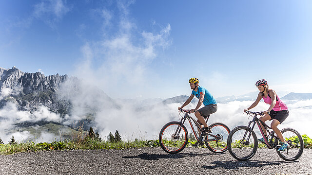 Zwei Radfahrer:innen vor Bergkulisse