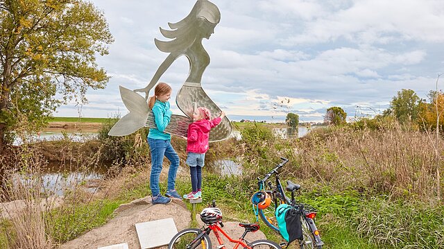 Zwei Kinder stehen an einer Meerjungfrauen-Statue