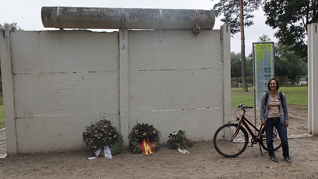 Autorin neben einem Stück alter Mauer und Kränzen