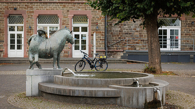 Kunstwerk an einem Brunnen, dahinter steht ein Fahrrad