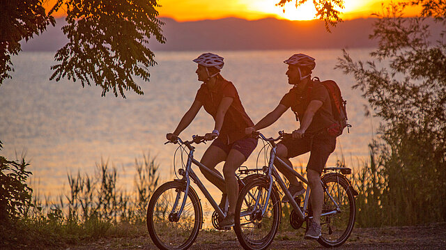 Radfahrer:innen am See bei Sonnenuntergang