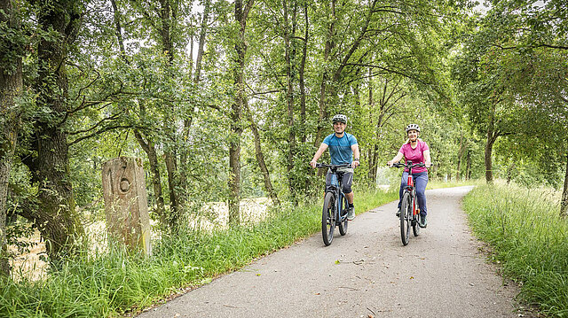 Zwei Radfahrer auf einem Radweg entlang Flussufer