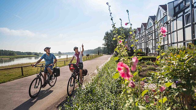 Ein Rad-Paar fährt auf einem Weg vorbei an Fachwerkhäusern
