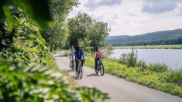 3 Radfahrer auf einem Radweg am Fluss
